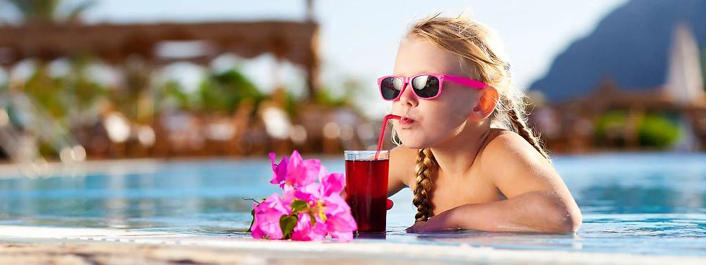 Mädchen mit Sonnenbrille trinkt Getränk aus Strohhalm am Pool 