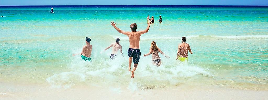 Fünf Urlauber rennen ins Meer und Wasser spritzt auf